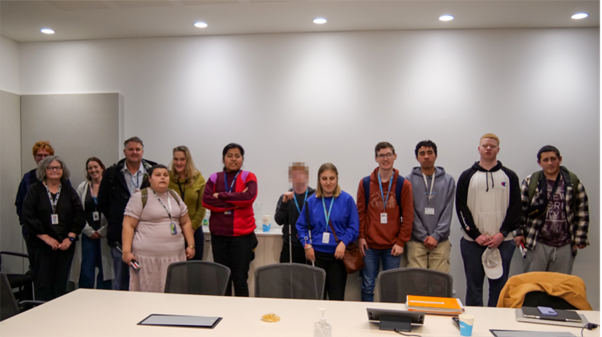 A group of people, some with white canes standing in a well-lit boardroom, smiling for the camera.