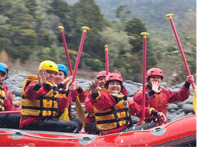 Four people in a red inflatable raft on a river, smiling for the camera.