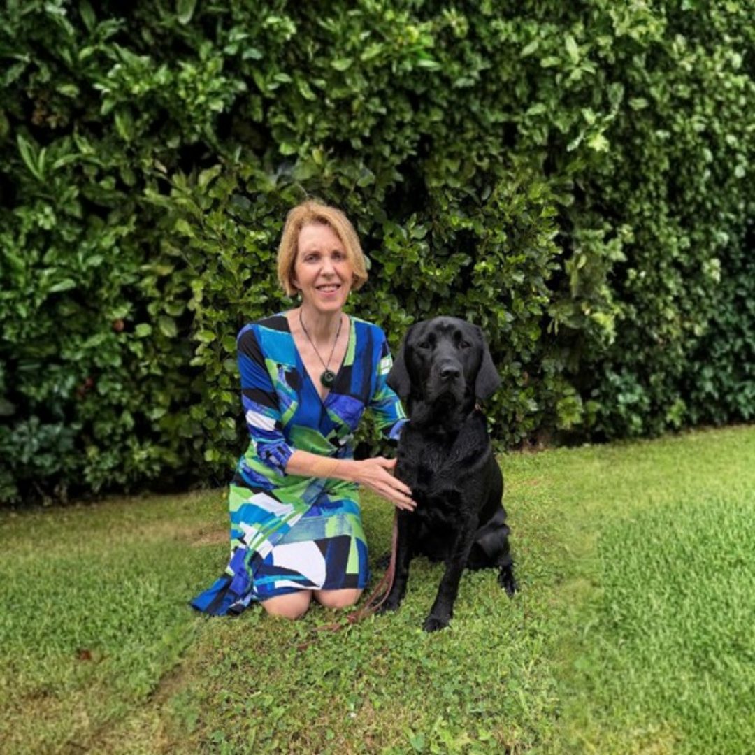 A woman sitting on grass with a guide dog. 