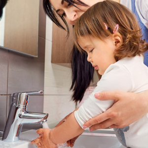 A child washes their hands at a sink while a woman stands next to them.