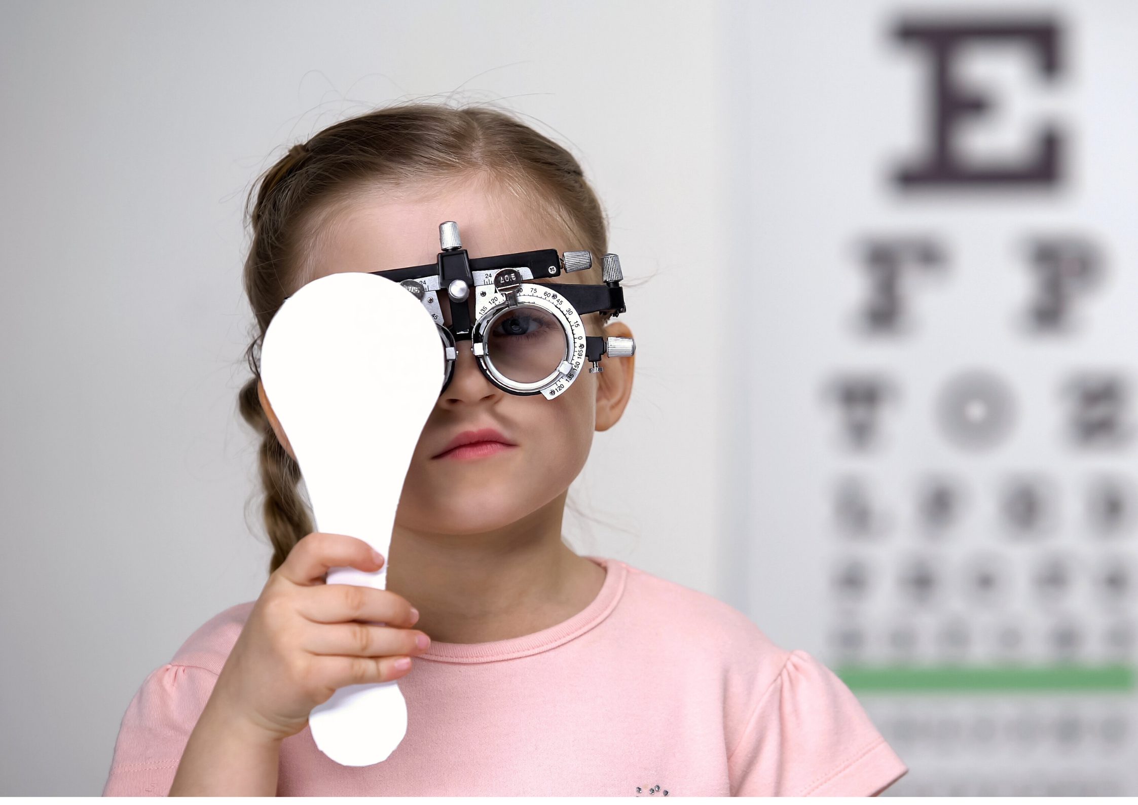 A young girl wearing vision-testing glasses covers one eye for an eye test. 