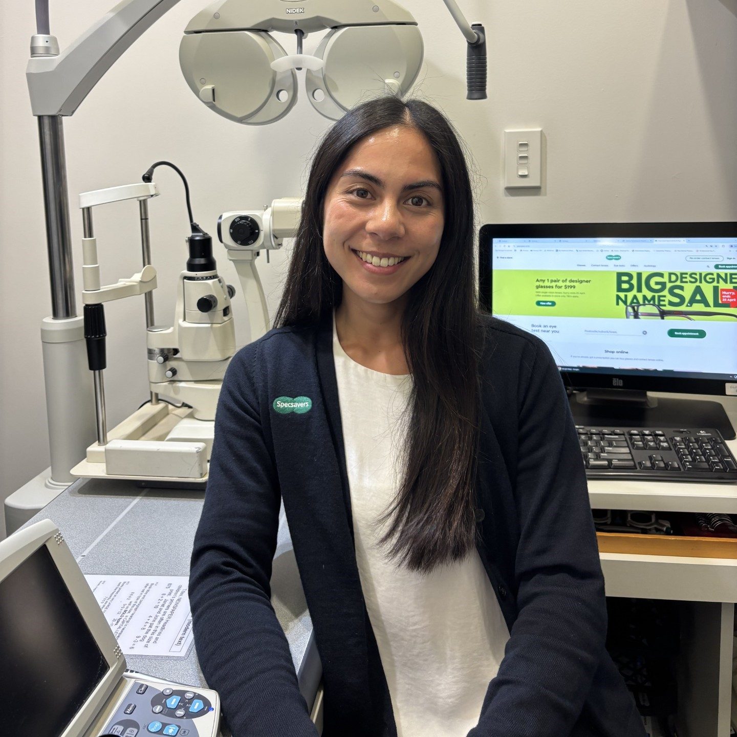 Woman in a navy blue jumper, it has a Specsavers logo on it.