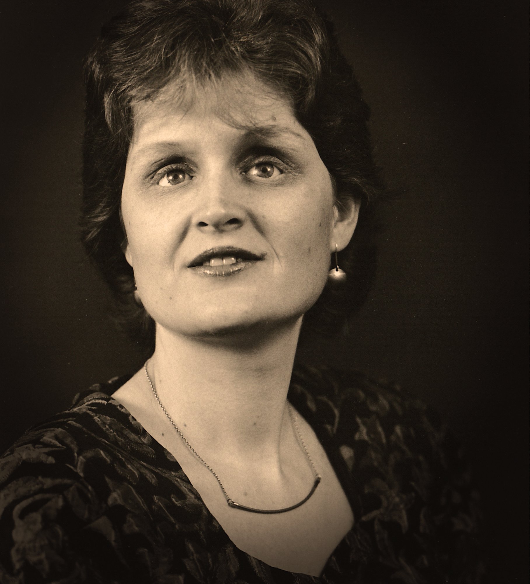 Sepia-toned portrait photo showing a middle-aged woman facing camera against a dark background.